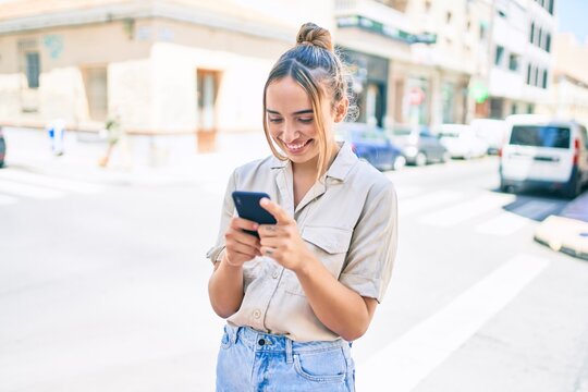 Young beautiful blonde caucasian woman smiling happy outdoors on a sunny day using smartphone
