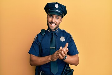 Handsome hispanic man wearing police uniform clapping and applauding happy and joyful, smiling proud hands together