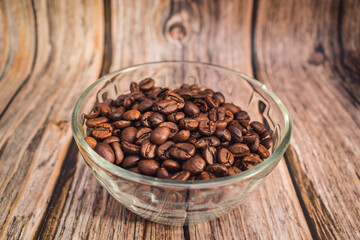 Freshly roasted coffee beans lie in a transparent glass vase on a wooden table