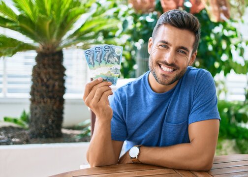Young hispanic man smiling happy holding australian dollars banknotes at the terrace.