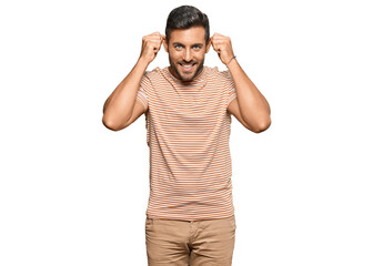 Handsome hispanic man wearing casual clothes smiling pulling ears with fingers, funny gesture....