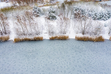 Shore area at a lake - wintry scenery - with a bizarre ice structure on a water surface and snow-covered shoreline after an ice-cold night in winter - aerial view 