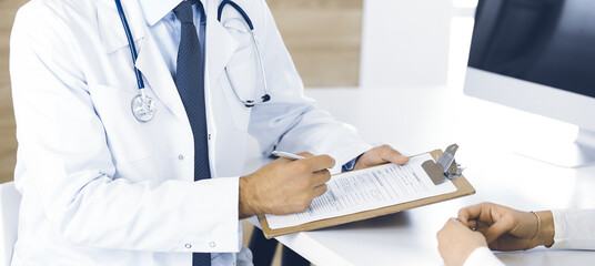 Doctor and patient discussing medical exam results while sitting at the desk in clinic, close-up....