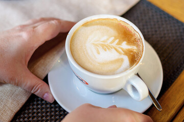 Cup of cappuccino with latte art. Beautiful foam, white cups. Hands in shot.