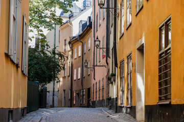 Obraz premium A narrow street with cobblestone pavement and colourful houses in the old part of Stockholm city - Gamla Stan. The bike is parked on the side and the windows face each other.