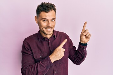 Young hispanic man wearing casual clothes smiling and looking at the camera pointing with two hands and fingers to the side.