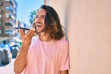 Fototapeta premium Young hispanic man smiling happy talking on the smartphone leaning on the wall