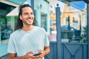 Young hispanic man smiling happy using smartphone at city.