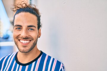 Young hispanic man smiling happy looking to the camera leaning on the wall