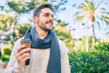 Young hispanic man smiling happy drinking take away coffee walking at the park.