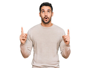 Fototapeta premium Young hispanic man wearing casual clothes amazed and surprised looking up and pointing with fingers and raised arms.