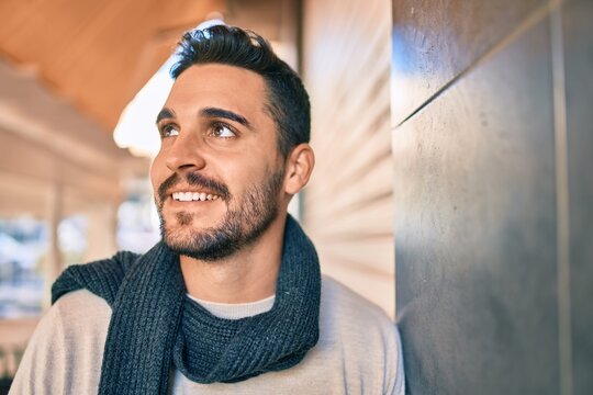 Young hispanic man smiling happy wearing scarf leaning on the wall at the city.