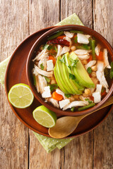 Caldo Tlalpeno is a delightful and nutritious soup made with chicken, carrots, chickpeas, and green beans closeup in the plate on the table. Vertical top view from above