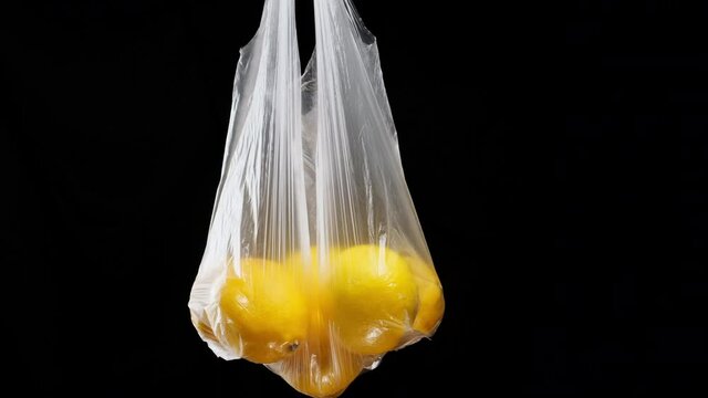Ripe yellow lemons lie in a transparent plastic bag on a black background, close up