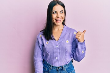 Young brunette woman wearing spring cardigan with flowers print pointing thumb up to the side...