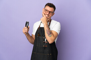 Barber caucasian man in an apron isolated on purple background happy and smiling