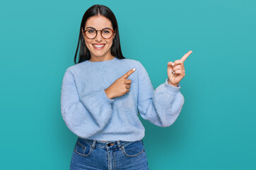 Young hispanic woman wearing casual clothes and glasses smiling and looking at the camera pointing with two hands and fingers to the side. - obrazy, fototapety, plakaty
