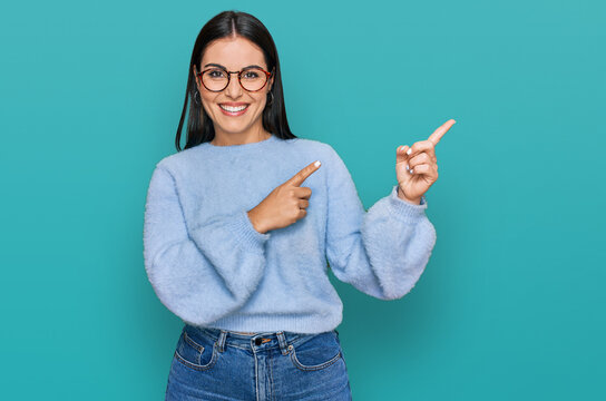 Young hispanic woman wearing casual clothes and glasses smiling and looking at the camera pointing with two hands and fingers to the side.
