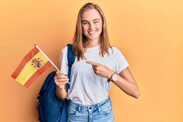Beautiful blonde woman exchange student holding spanish flag smiling happy pointing with hand and finger