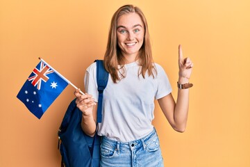 Beautiful blonde woman exchange student holding australia flag smiling with an idea or question pointing finger with happy face, number one © Krakenimages.com