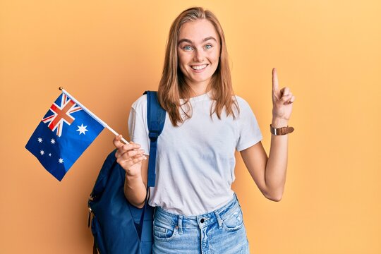 Beautiful blonde woman exchange student holding australia flag smiling with an idea or question pointing finger with happy face, number one