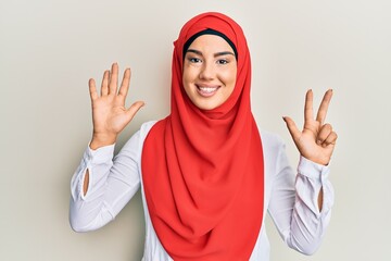 Young beautiful hispanic girl wearing traditional islamic hijab scarf showing and pointing up with fingers number eight while smiling confident and happy.