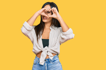 Young beautiful hispanic girl wearing casual clothes doing heart shape with hand and fingers smiling looking through sign