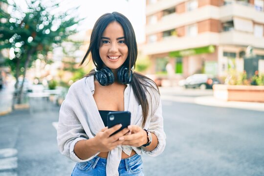 Young hispanic girl smiling happy using smartphone and headphones at the city.