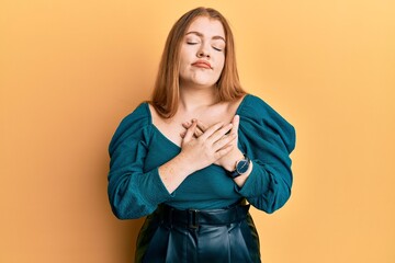 Young beautiful redhead woman wearing elegant and sexy look smiling with hands on chest with closed eyes and grateful gesture on face. health concept.