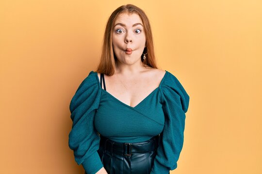 Young beautiful redhead woman wearing elegant and sexy look making fish face with lips, crazy and comical gesture. funny expression.