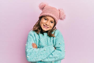 Little beautiful girl wearing wool sweater and cute winter hat happy face smiling with crossed arms looking at the camera. positive person.
