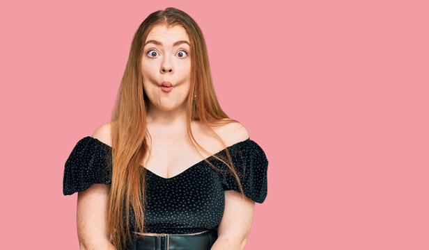 Young beautiful redhead woman wearing elegant clothes making fish face with lips, crazy and comical gesture. funny expression.