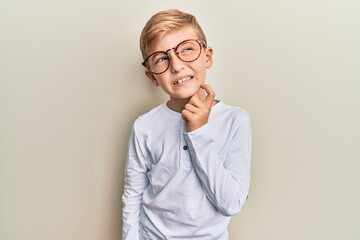 Little caucasian boy kid wearing casual clothes and glasses thinking concentrated about doubt with finger on chin and looking up wondering