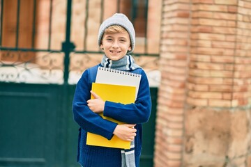 Adorable blond student kid smiling happy holding book at the school.