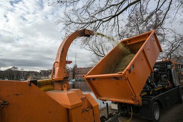 Professional heavy duty shredding machine blows the shredded twigs into a dump truck, during tree...