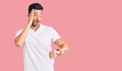 Young handsome hispanic man wearing casual clothes looking at the watch time worried, afraid of...
