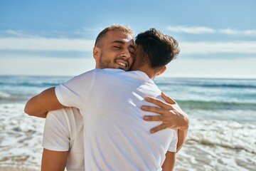 Young gay couple smiling happy hugging at the beach.