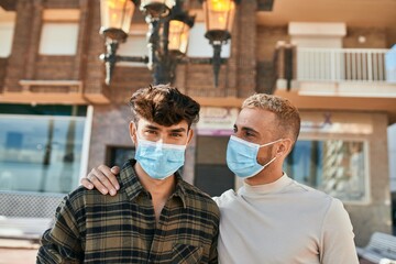 Fototapeta na wymiar Young gay couple wearing medical mask hugging at the city.