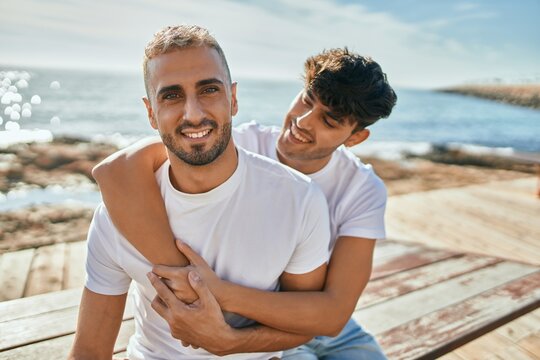 Young gay couple smiling happy sitting on the bench at the beach promenade.
