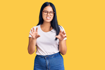 Young beautiful asian girl wearing casual clothes and glasses smiling funny doing claw gesture as cat, aggressive and sexy expression