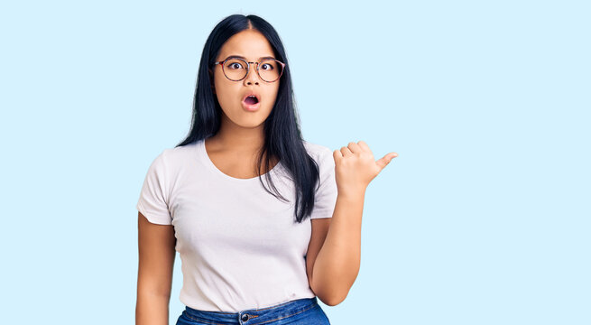 Young beautiful asian girl wearing casual clothes and glasses surprised pointing with hand finger to the side, open mouth amazed expression.
