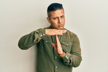 Young latin man wearing casual clothes doing time out gesture with hands, frustrated and serious...