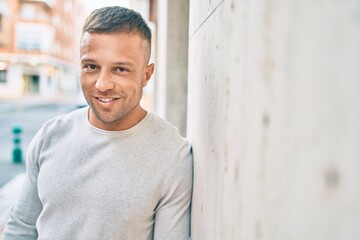 Obraz premium Young caucasian man smiling happy leaning on the wall at the city.