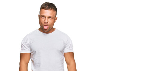 Handsome muscle man wearing casual white tshirt sticking tongue out happy with funny expression. emotion concept.