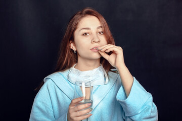 young woman on a black background holding a pill and a glass of water in her hands