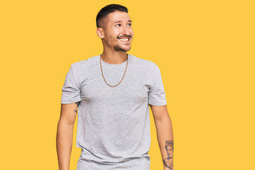 Handsome man with tattoos wearing 90s style looking away to side with smile on face, natural...