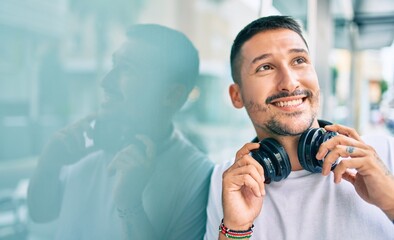 Young hispanic man smiling happy listening to music using headphones at street of city.