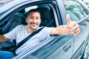 Young hispanic man smiling happy doing ok sign driving car.