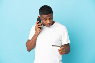 Young latin man isolated on blue background buying with the mobile with a credit card
