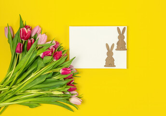 Easter frame of pink and red tulips and wooden bunny on yellow background. Top view with copy space. Happy Easter holiday. Greeting card.